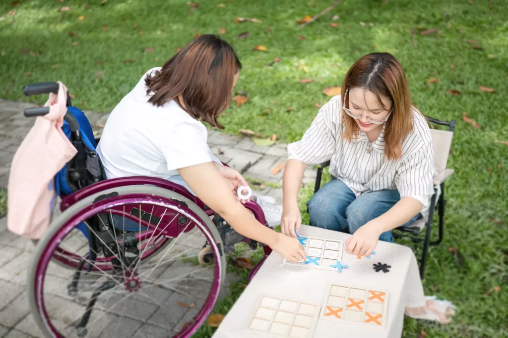 A disabled woman in a wheelchair is playing naughts and crosses with her care giver
